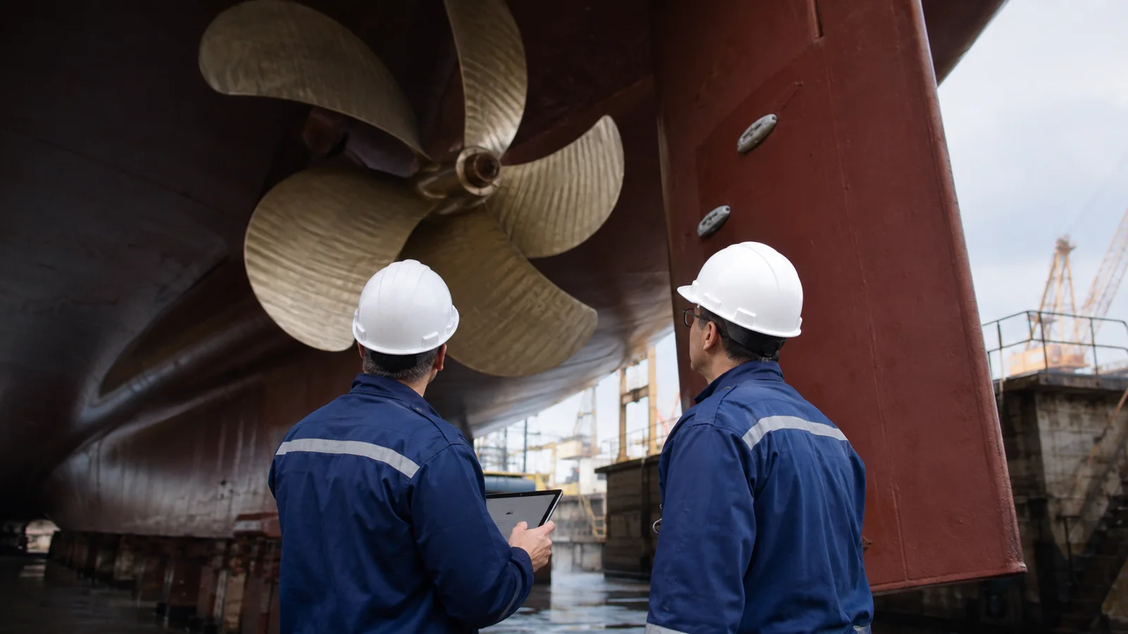 Surveyors inspecting a large propeller and rudder in dry dock