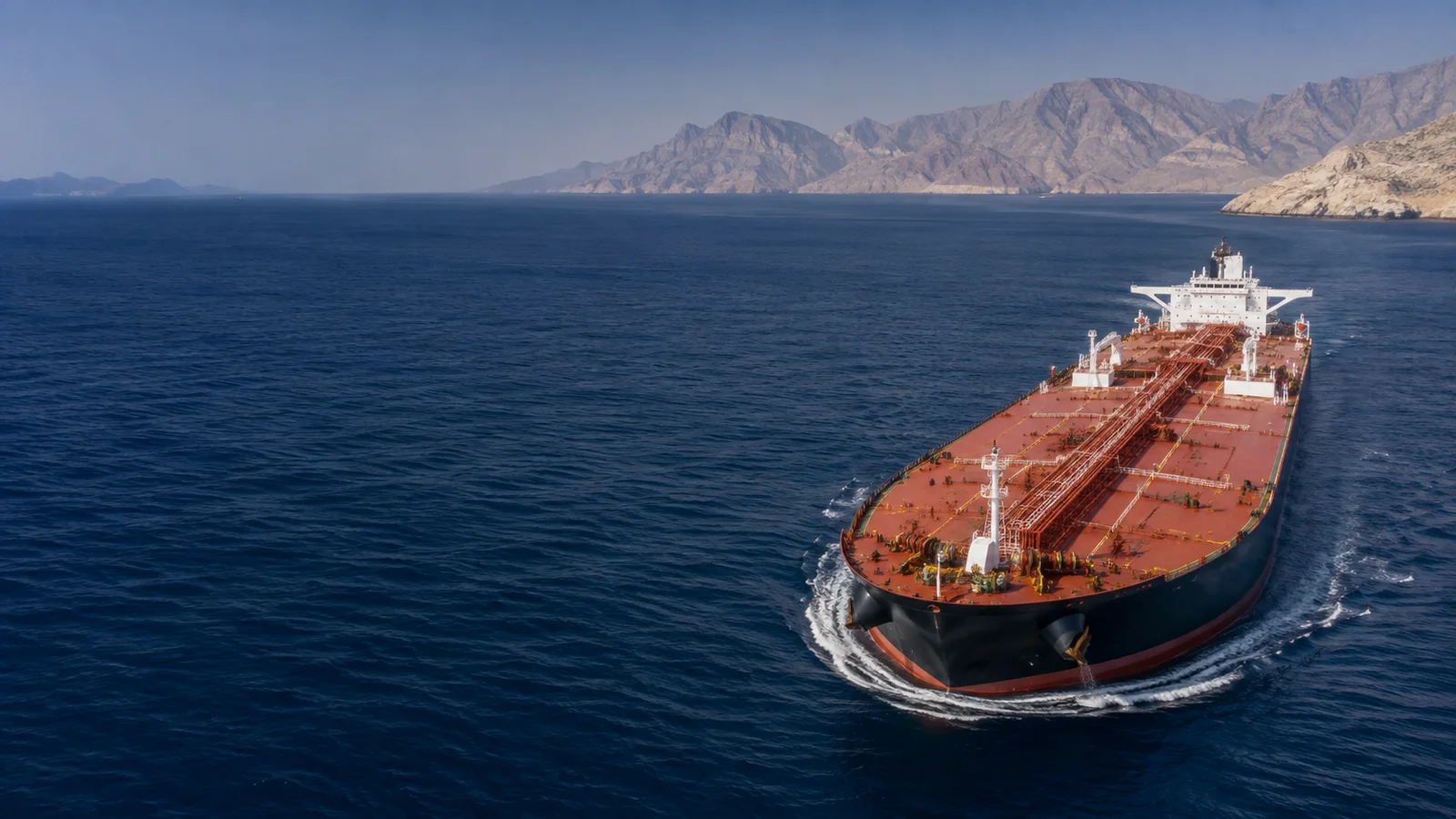 Oil tanker crossing blue Gulf waters with a mountainous coastline in the distance