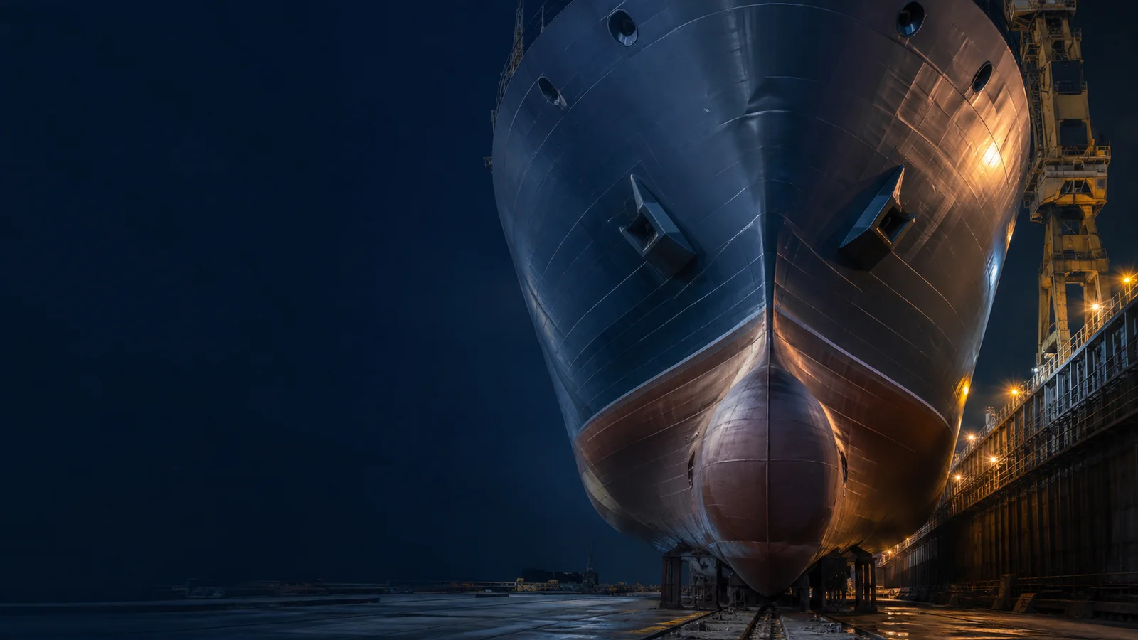Large commercial vessel hull in a dry dock under warm industrial lights